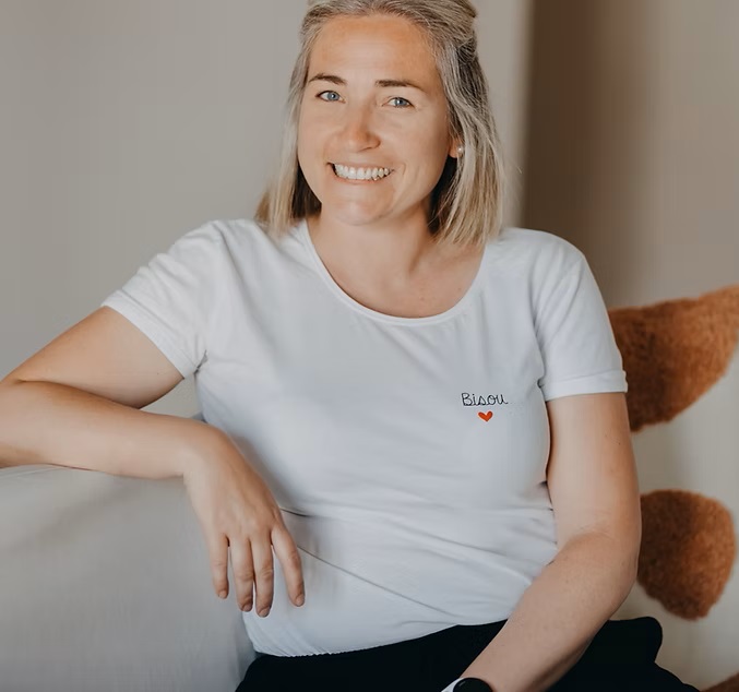 Elise Bernold, fondatrice de l’institut Entre Nous, souriante et détendue, assise sur un fauteuil, vêtue d’un t-shirt blanc