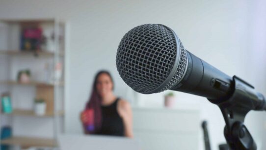 Microphone en premier plan avec Alexia Robert floue en arrière-plan dans son studio vocal à Gland.