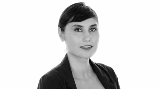 Portrait de Nassime Zafarsani, souriante en tenue professionnelle, sur fond blanc