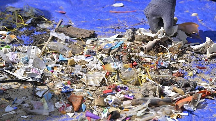 Main gantée ramassant des déchets plastiques et débris sur une plage, symbole de la pollution marine et de la nécessité de protéger les océans.