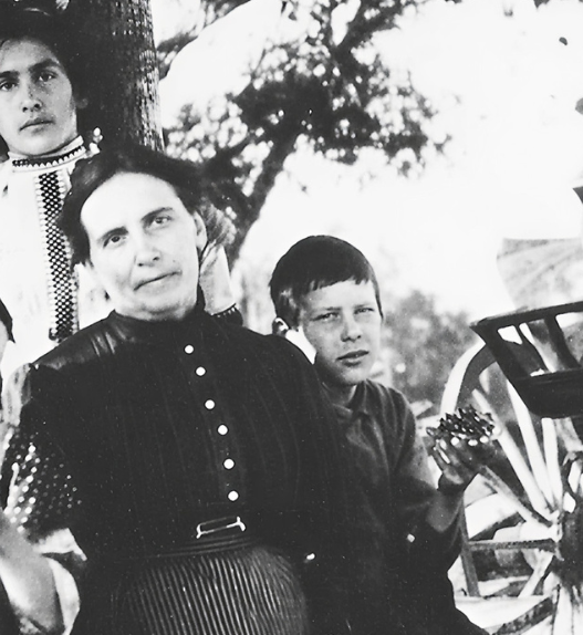 Photographie en noir et blanc d’Augusta Gillabert-Randin entourée de ses enfants, posant en plein air près d’une charrette agricole, au début du XXᵉ siècle.