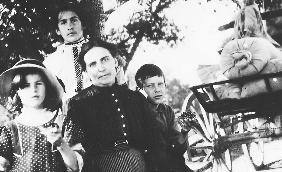 Photographie en noir et blanc d’Augusta Gillabert-Randin entourée de ses enfants, posant en plein air près d’une charrette agricole, au début du XXᵉ siècle.