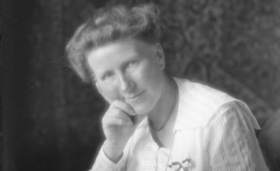 Portrait en noir et blanc d’Émilie Gourd, de trois-quarts, la tête légèrement inclinée et la main posée sous le menton, portant un chemisier clair. Elle regarde l’objectif avec une expression douce et réfléchie.