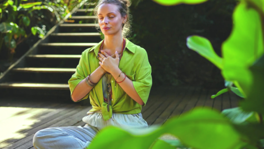 Femme assise en pleine nature, les yeux fermés et les mains posées sur la poitrine, illustrant un moment de respiration consciente et de régulation émotionnelle.
