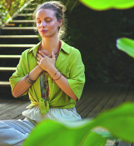 Femme assise en pleine nature, les yeux fermés et les mains posées sur la poitrine, illustrant un moment de respiration consciente et de régulation émotionnelle.