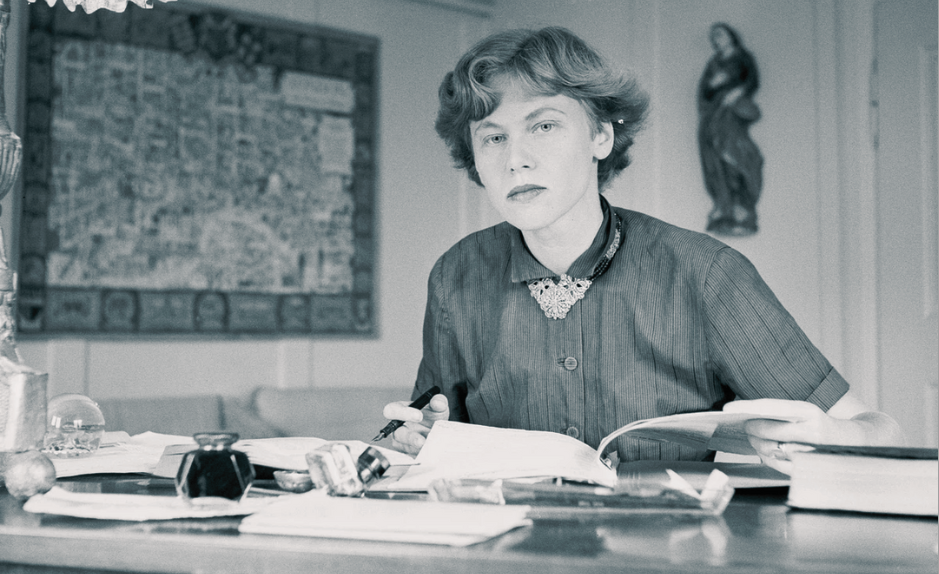 Iris von Roten assise à son bureau, écrivant et consultant des documents, dans un intérieur sobre, photographie en noir et blanc