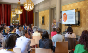 Atelier participatif lors de la Journée romande de l’égalité 2025 à Genève, avec une intervenante présentant un projet devant un public majoritairement féminin dans une salle historique.