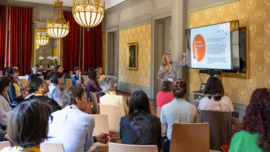 Atelier participatif lors de la Journée romande de l’égalité 2025 à Genève, avec une intervenante présentant un projet devant un public majoritairement féminin dans une salle historique.