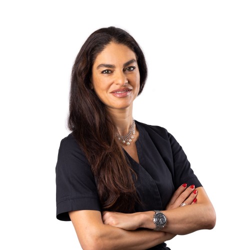 Portrait de Mouna Skaria, bras croisés, portant une blouse noire sur fond blanc.