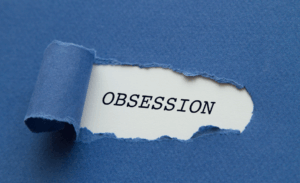 L’image montre un morceau de papier bleu déchiré, laissant apparaître un fond blanc où est inscrit le mot OBSESSION en lettres capitales noires