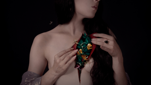 Autoportrait photographique d’Audrey Piguet montrant un buste féminin nu, la poitrine entrouverte révélant des fleurs et des feuilles, sur fond sombre.