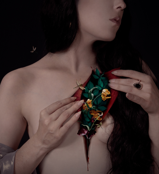 Autoportrait photographique d’Audrey Piguet montrant un buste féminin nu, la poitrine entrouverte révélant des fleurs et des feuilles, sur fond sombre.