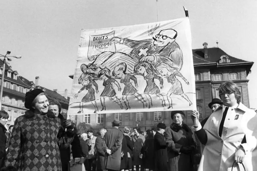 Manifestation pour le droit de vote des femmes à Berne en 1969, avec une banderole caricaturant le pouvoir masculin et la revendication d’égalité.
