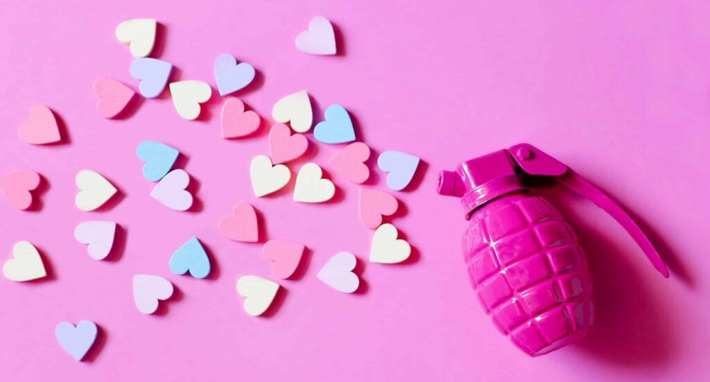 Cœurs colorés projetés hors d’une grenade rose, illustrant le love bombing et la manipulation émotionnelle dans les relations en ligne.