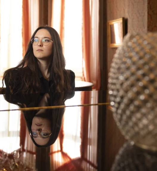 Veronica Fusaro assise au piano dans un intérieur élégant, reflet sur le clavier, lumière naturelle en arrière-plan.