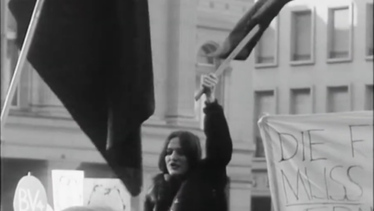 Manifestation féministe en Suisse devant un bâtiment officiel, une femme brandit un drapeau lors d’un rassemblement pour les droits des femmes.