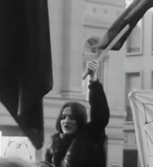 Manifestation féministe en Suisse devant un bâtiment officiel, une femme brandit un drapeau lors d’un rassemblement pour les droits des femmes.