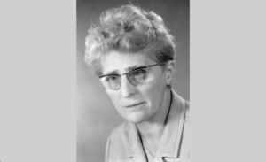 Portrait en noir et blanc d’Emma Kammacher, avocate et femme politique genevoise, portant des lunettes, photographiée de face sur fond neutre, milieu du XXᵉ siècle.