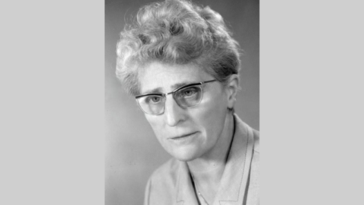 Portrait en noir et blanc d’Emma Kammacher, avocate et femme politique genevoise, portant des lunettes, photographiée de face sur fond neutre, milieu du XXᵉ siècle.