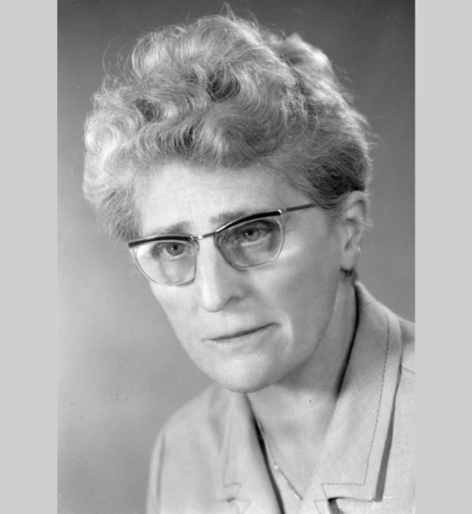 Portrait en noir et blanc d’Emma Kammacher, avocate et femme politique genevoise, portant des lunettes, photographiée de face sur fond neutre, milieu du XXᵉ siècle.