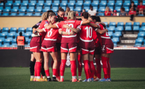 Équipe de football féminin suisse rassemblée en cercle sur le terrain avant un match, symbolisant la cohésion et l’essor du football féminin en Suisse.