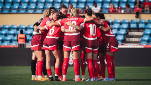 Équipe de football féminin suisse rassemblée en cercle sur le terrain avant un match, symbolisant la cohésion et l’essor du football féminin en Suisse.