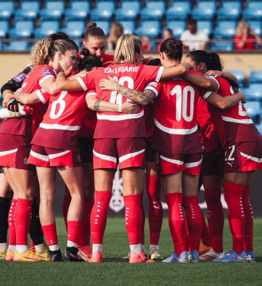 Équipe de football féminin suisse rassemblée en cercle sur le terrain avant un match, symbolisant la cohésion et l’essor du football féminin en Suisse.