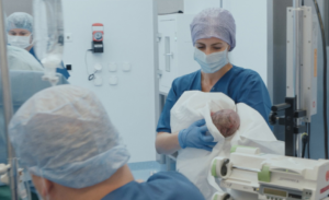 Sage-femme en salle d’accouchement tenant un nouveau-né dans un hôpital suisse, extrait du documentaire Sages-femmes – Voir le jour.