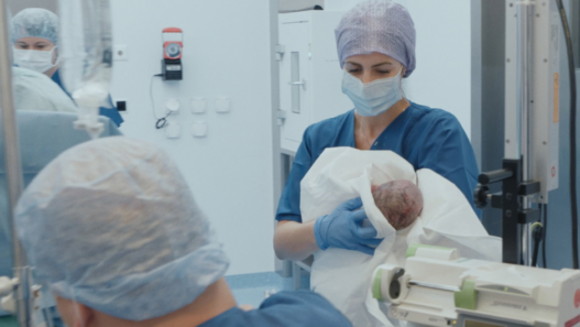 Sage-femme en salle d’accouchement tenant un nouveau-né dans un hôpital suisse, extrait du documentaire Sages-femmes – Voir le jour.