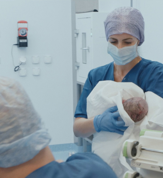 Sage-femme en salle d’accouchement tenant un nouveau-né dans un hôpital suisse, extrait du documentaire Sages-femmes – Voir le jour.