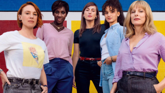 Image promotionnelle du film « La Maison des femmes » : cinq femmes debout, solidaires, devant un fond jaune, bleu et rouge.