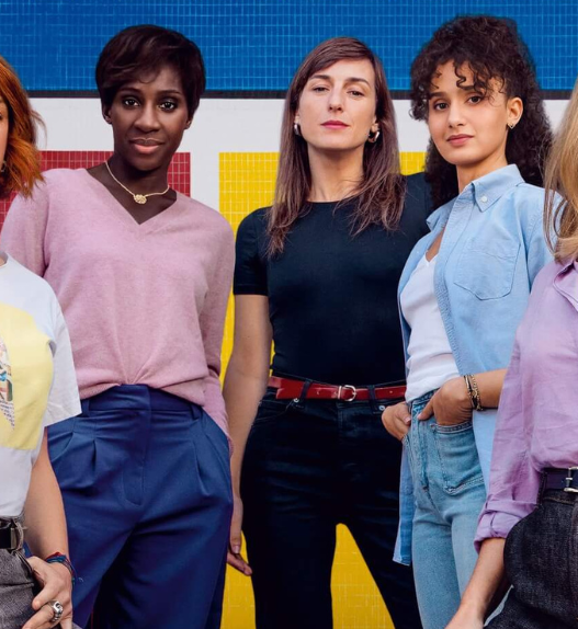 Image promotionnelle du film « La Maison des femmes » : cinq femmes debout, solidaires, devant un fond jaune, bleu et rouge.