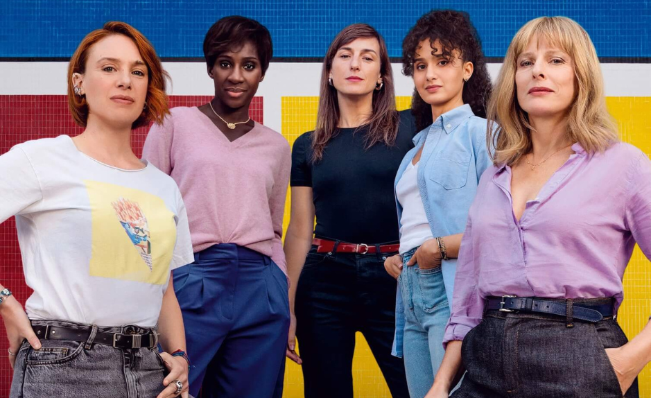 Image promotionnelle du film « La Maison des femmes » : cinq femmes debout, solidaires, devant un fond jaune, bleu et rouge.