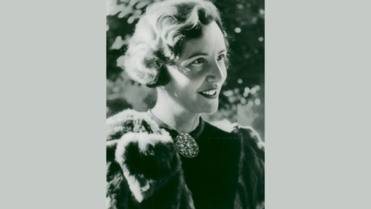 Portrait en noir et blanc d’Antoinette Quinche, juriste suisse et figure du suffrage féminin, souriante en tenue élégante.