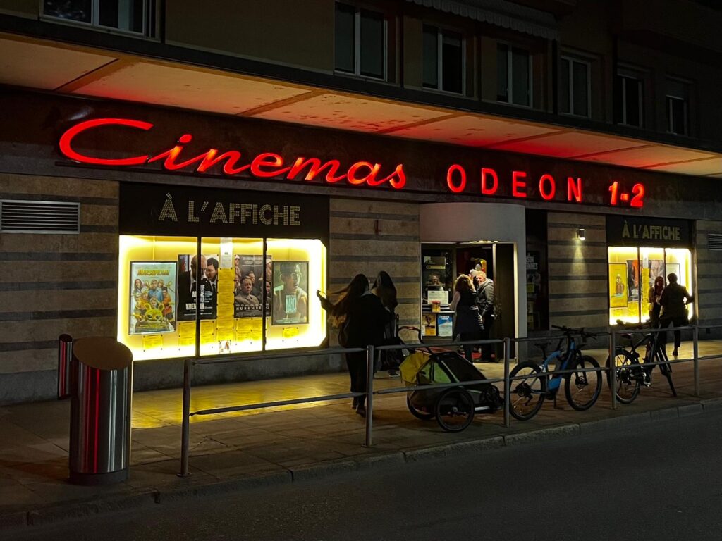 Façade nocturne du Cinéma Odéon à Morges, avec des spectateurs entrant pour la projection du film « La Maison des femmes ».