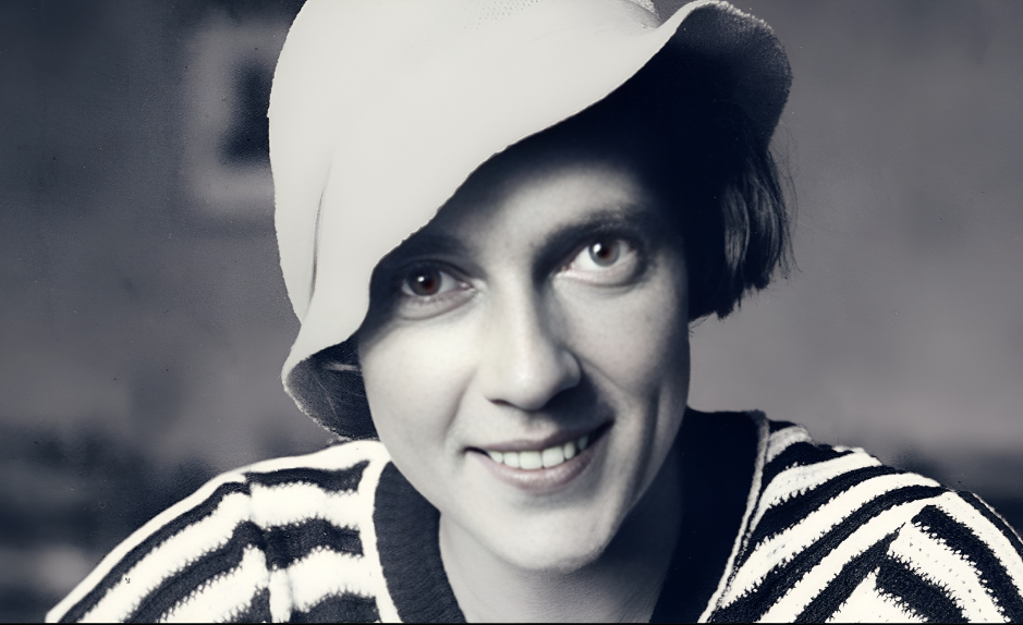 Portrait en noir et blanc d’Ella Maillart jeune, souriante, portant un chapeau clair et un pull rayé