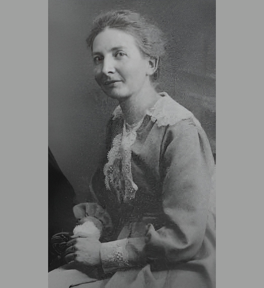 Portrait d’Hélène Monastier, enseignante vaudoise et figure du pacifisme en Suisse romande, assise en robe claire, début du XXe siècle.