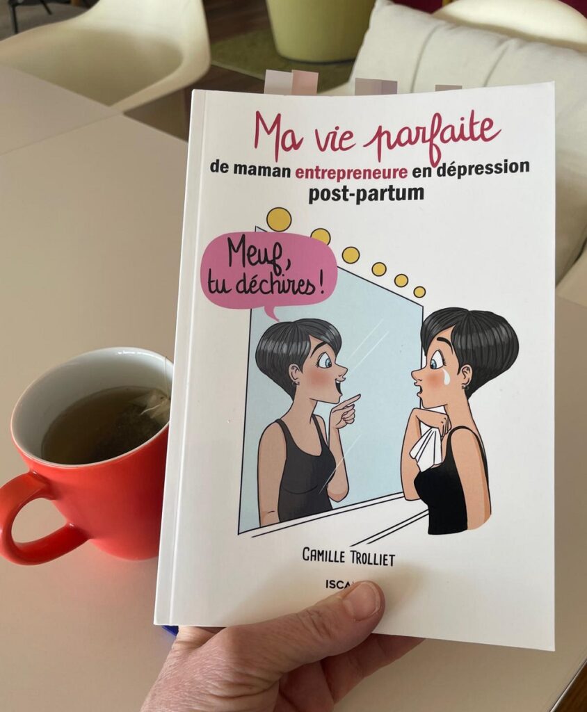 Livre "Ma vie parfaite : de maman entrepreneure en dépression post-partum" de Camille Trolliet tenu en main sur une table avec une tasse de thé.