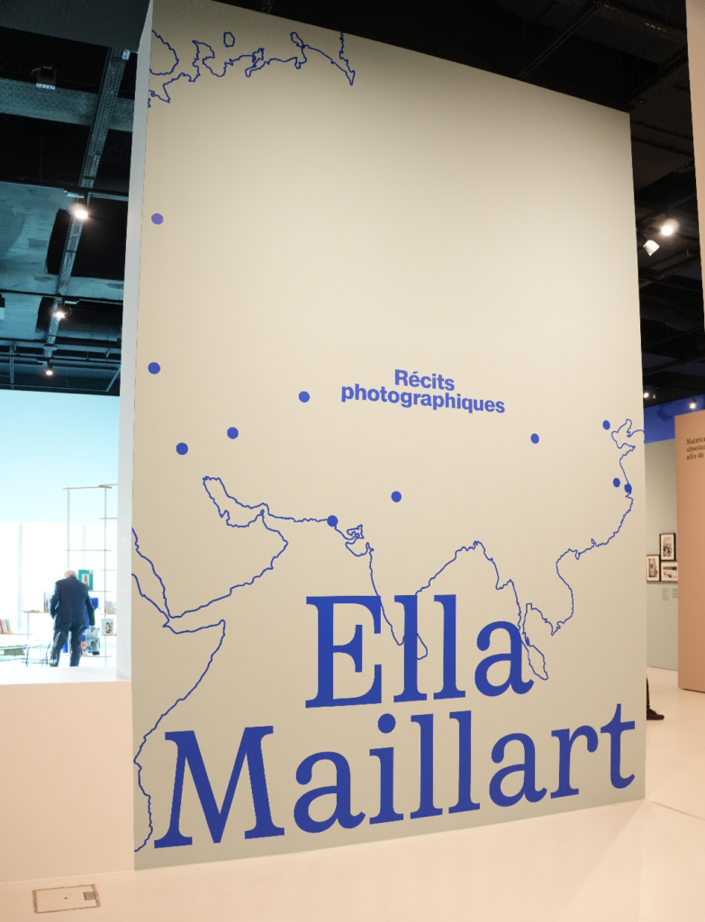 Panneau d’exposition à Photo Elysée avec le titre « Ella Maillart » et « Récits photographiques », sur fond de carte stylisée en bleu avec des points représentant des étapes de voyage.