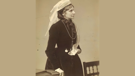 Portrait photographique ancien en sépia de Josephine Butler posant de profil, tournée vers la droite. Elle porte une robe sombre à manches longues boutonnée sur le devant, un ruban noué au cou, un long collier de perles et un voile clair translucide drapé sur sa tête et ses épaules.
