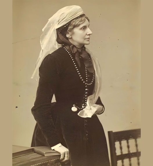Portrait photographique ancien en sépia de Josephine Butler posant de profil, tournée vers la droite. Elle porte une robe sombre à manches longues boutonnée sur le devant, un ruban noué au cou, un long collier de perles et un voile clair translucide drapé sur sa tête et ses épaules.