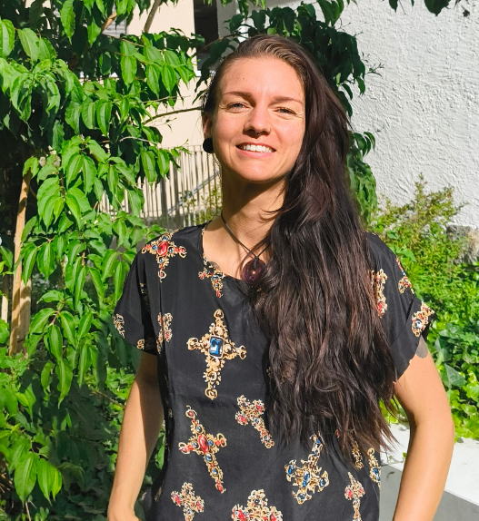 Portrait de Soraya Poulin souriante en extérieur, devant des plantes vertes et un mur blanc.