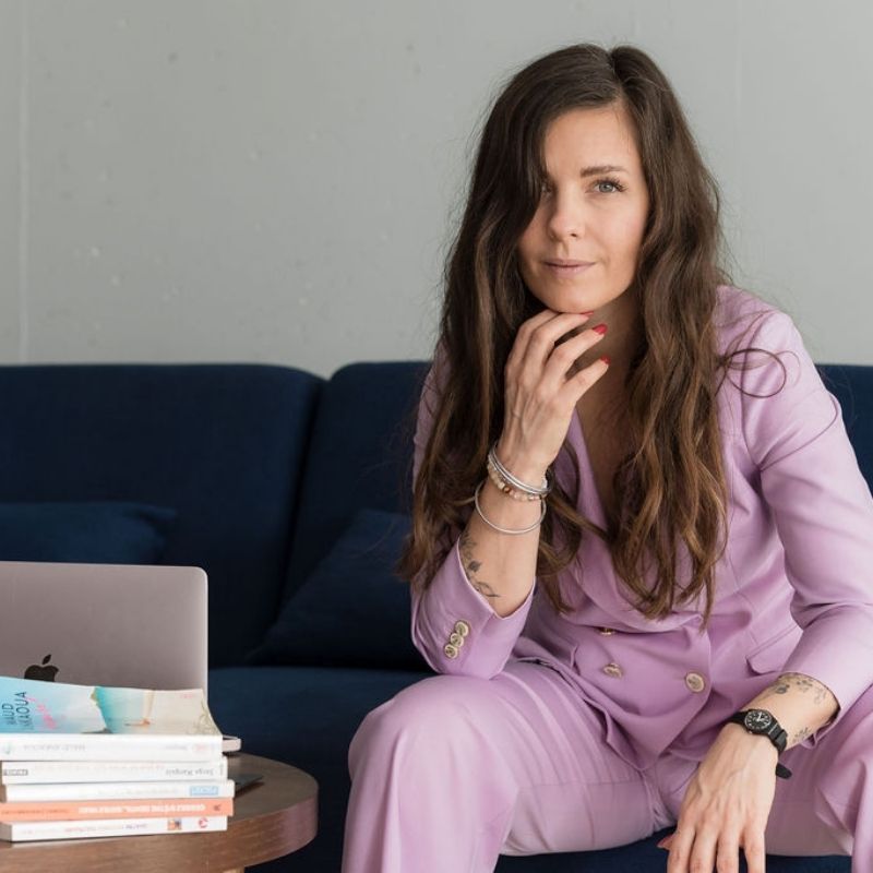 Portrait d’Isaline Ackermann, coach de vie et podcasteuse suisse, assise sur un canapé avec un ordinateur et des livres.