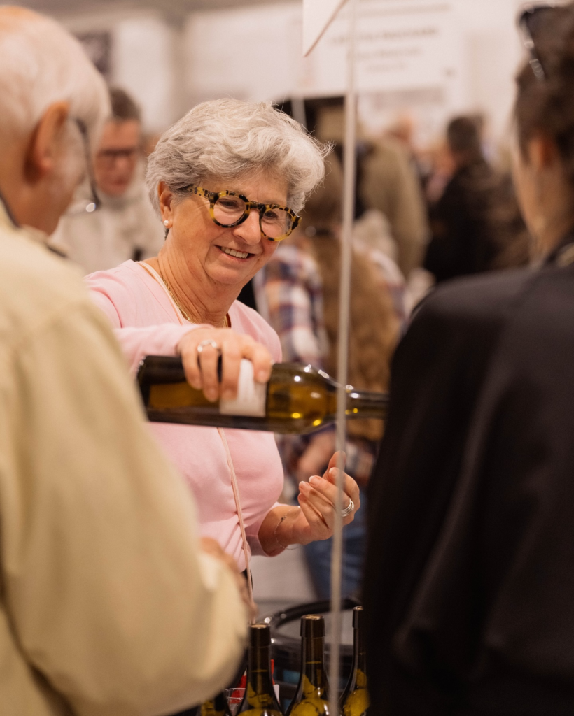 Coraline de Wurstemberger, fondatrice de DiVINes !, souriante, sert du vin à des visiteurs lors d'une dégustation.