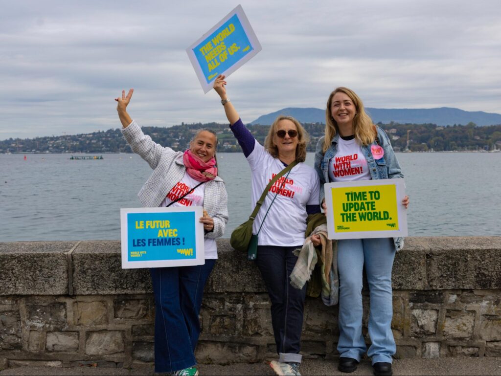 Trois participantes à World with Women présentent des pancartes pour l’égalité au bord du lac à Genève.