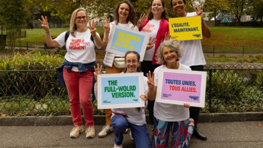 Six participantes à World with Women Switzerland posant dans un parc avec des pancartes en faveur de l’égalité.