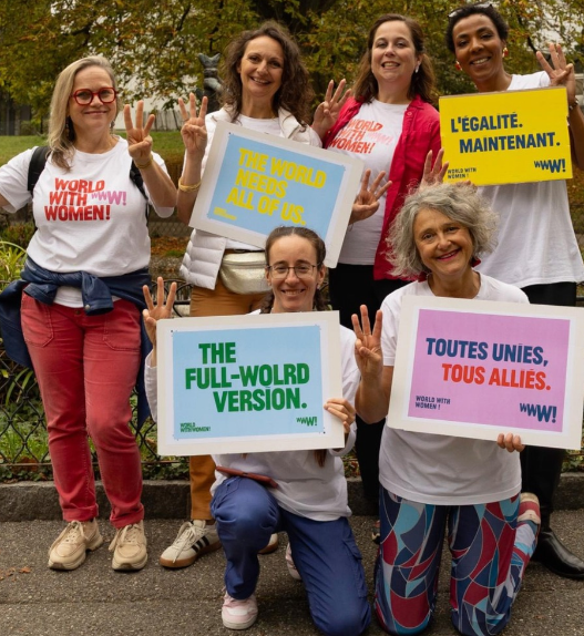 Six participantes à World with Women Switzerland posant dans un parc avec des pancartes en faveur de l’égalité.