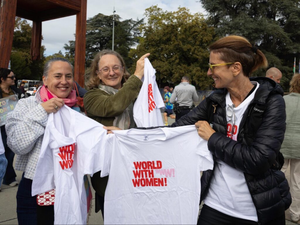 Trois participantes à World with Women Switzerland présentant des tee-shirts du mouvement lors du rassemblement à Genève.